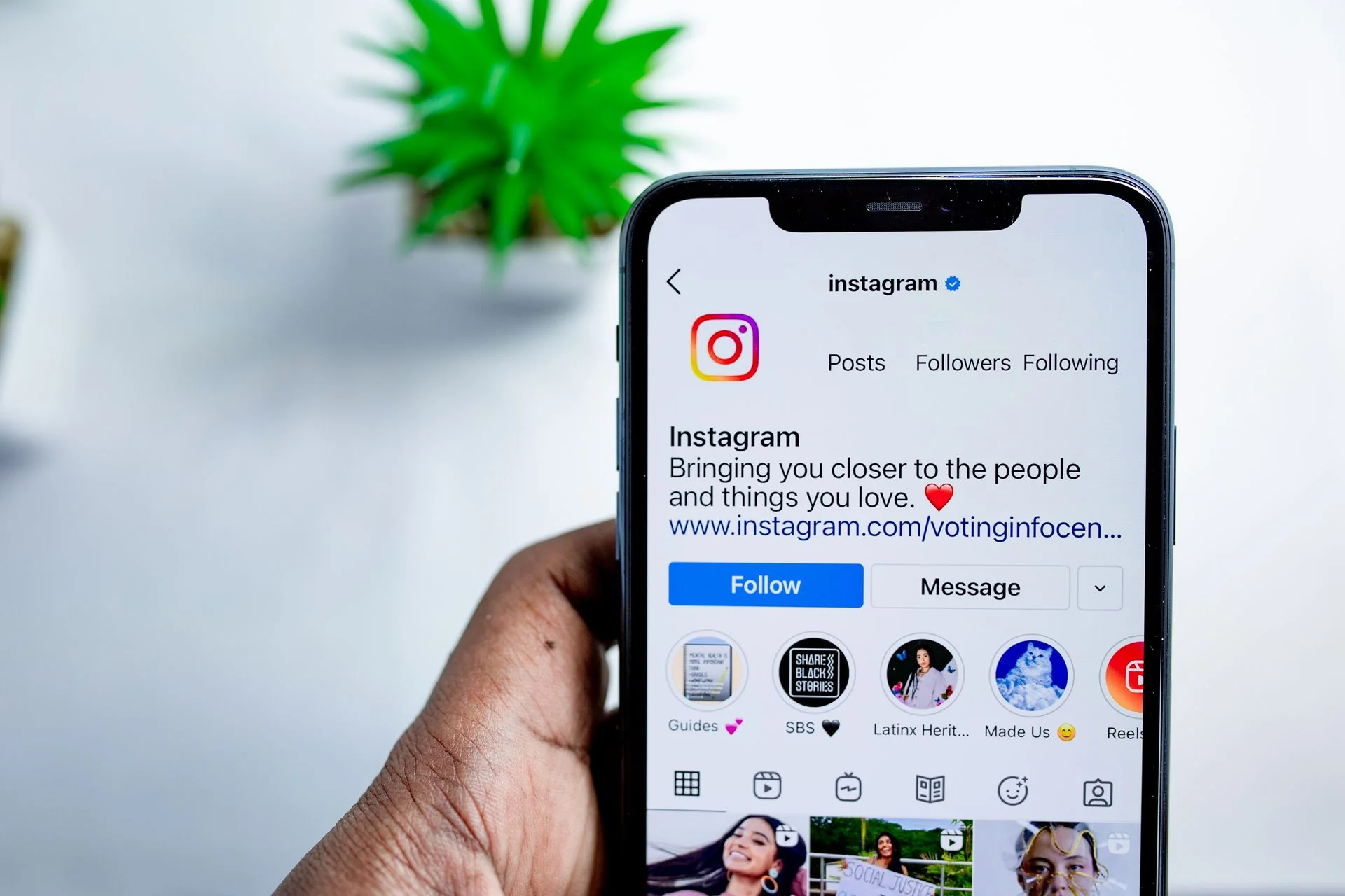 A hand holds a phone showing an Instagram profile with a visible Message button.