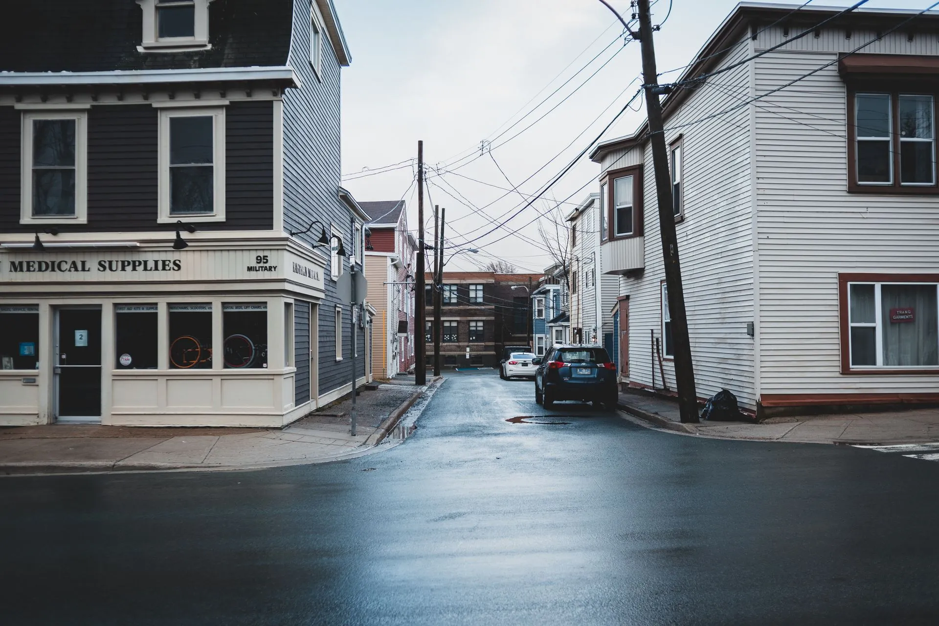 Neighborhood intersection with a medical-supply storefront and houses along a side street.