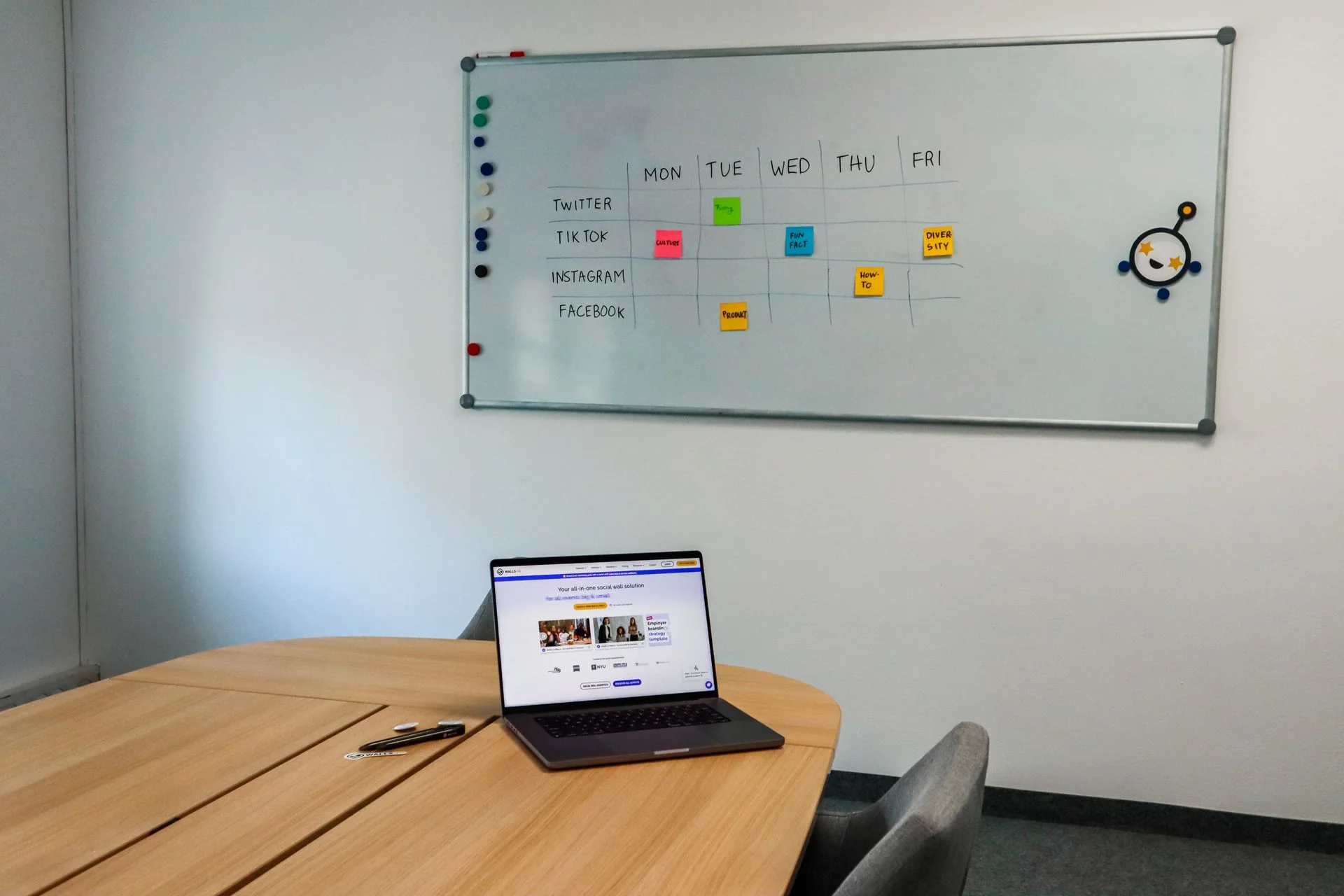 A whiteboard organizes social posts by channel and weekday above a laptop on a meeting table.