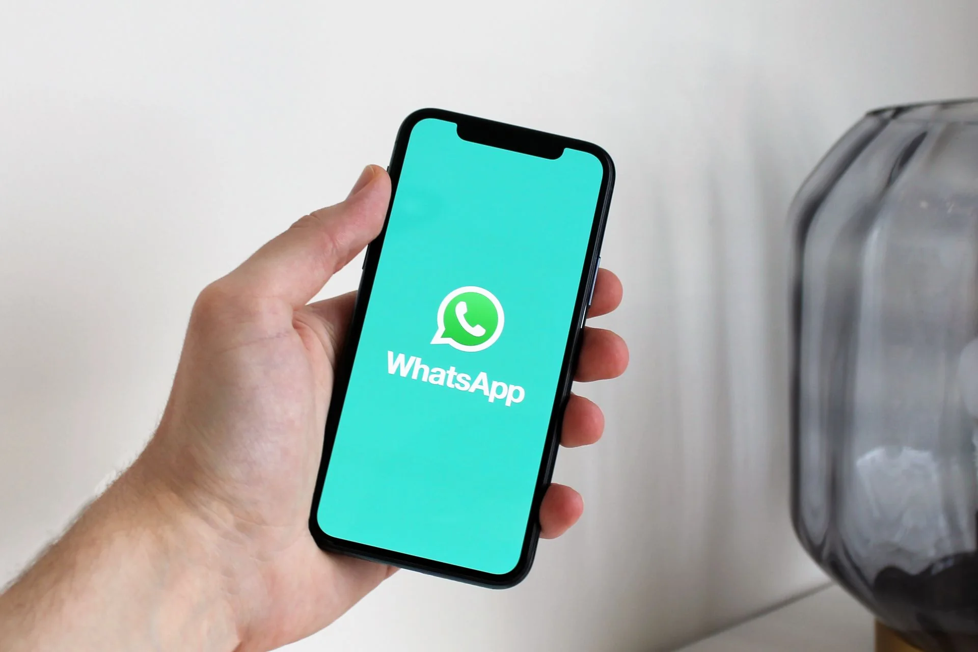 A hand holds a smartphone displaying the WhatsApp logo on a turquoise screen.